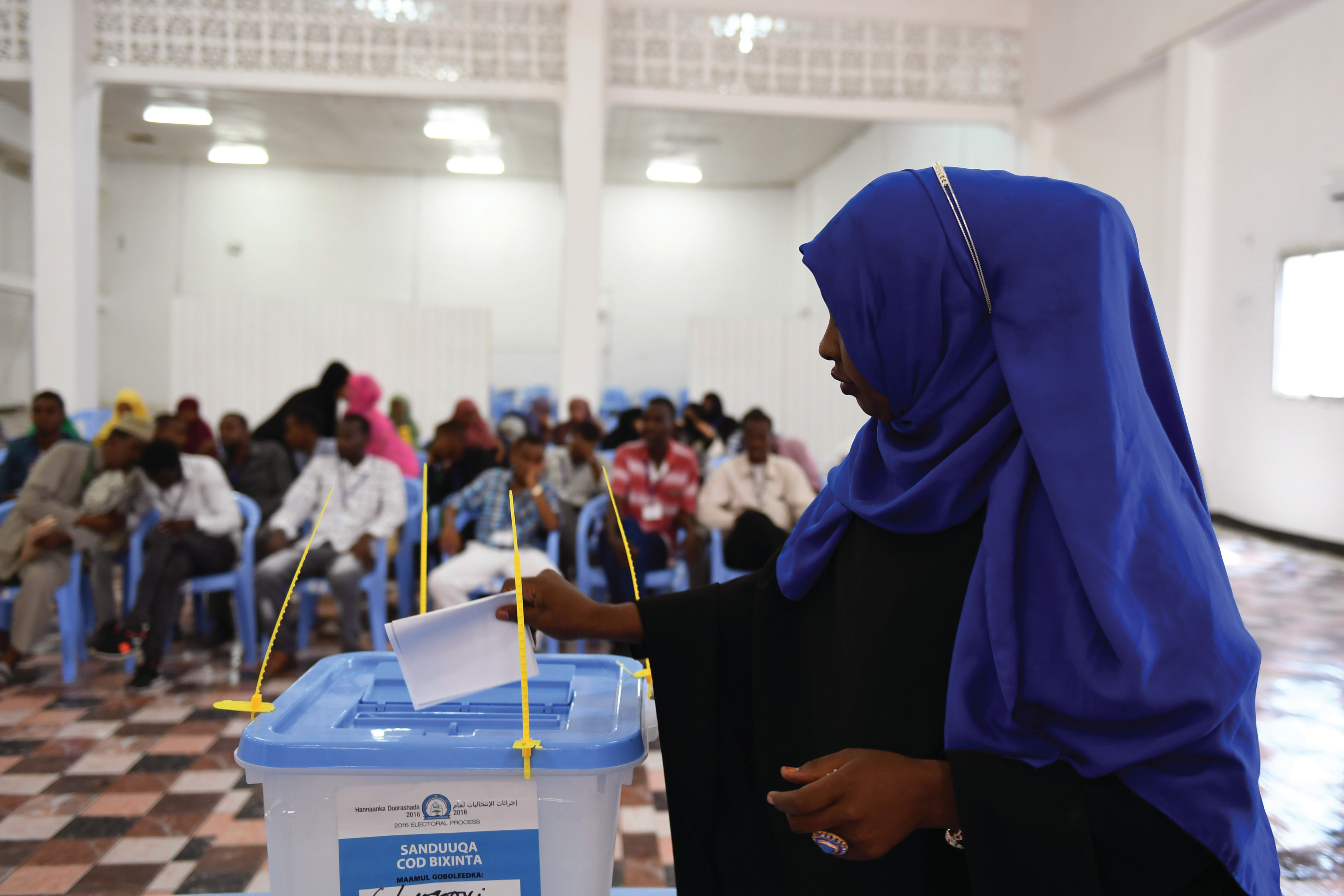 A young woman wearing a blue headscarf places her balot into a sealed plastic bin.