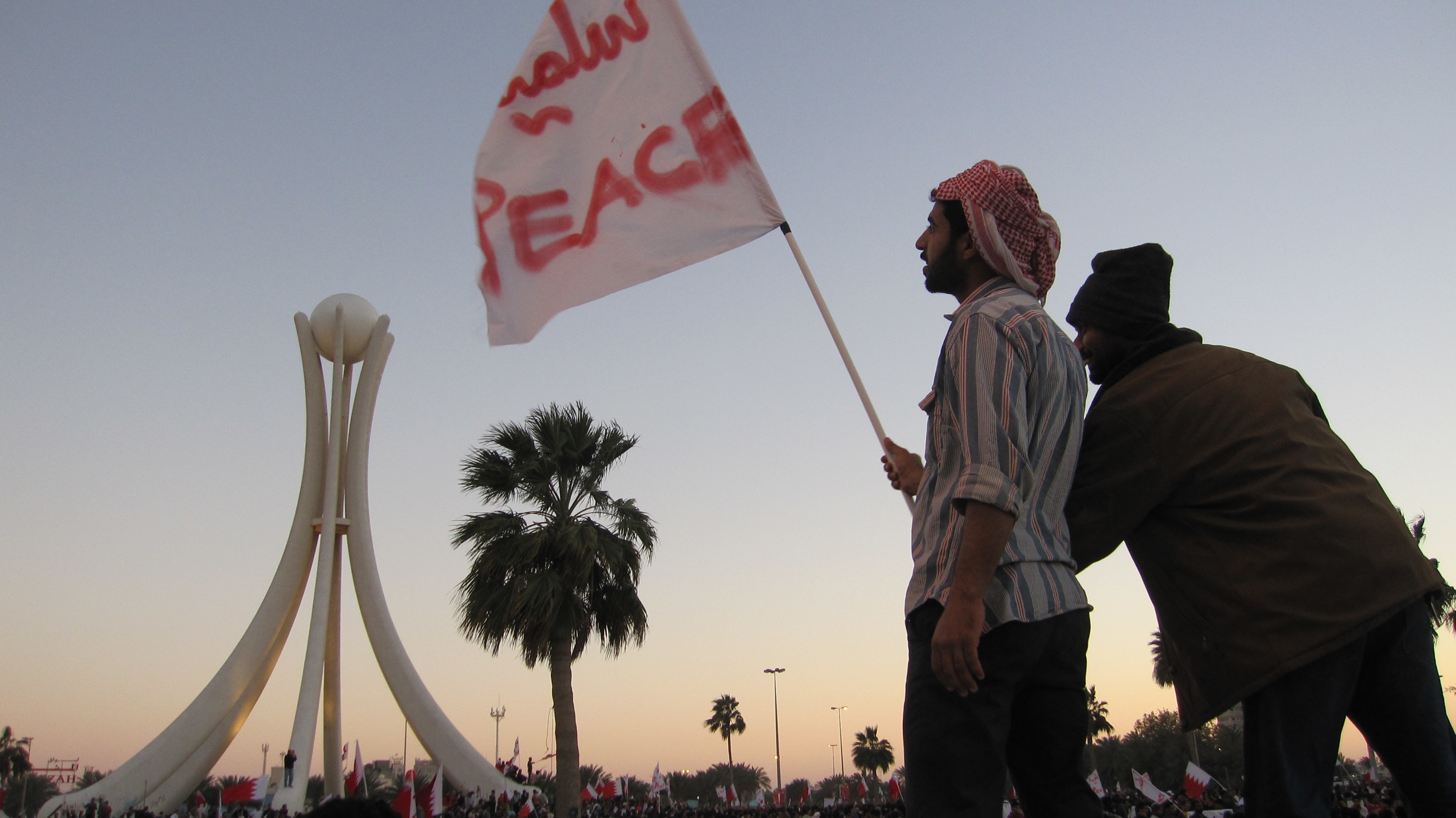 Men stand atop a car with a flag that says "PEACE" in Arabic and English.